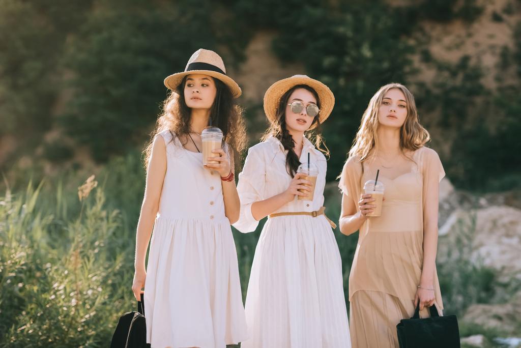 όμορφα κορίτσια σε κομψό άχυρο καπέλα ψάθινο καπέλο κρατώντας καφέ latte - Φωτογραφία, εικόνα