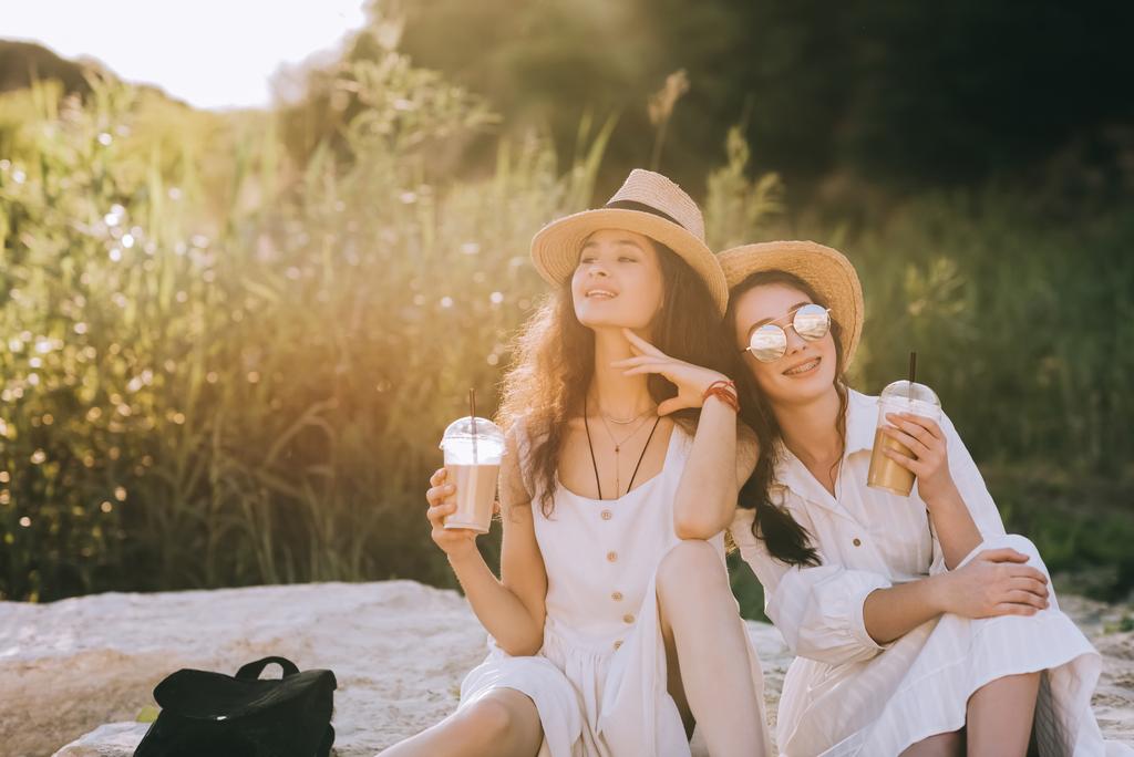 mooie gelukkige vrienden met kopjes koffie latte zittend op de grond met zonlicht - Foto, afbeelding