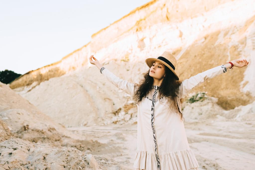 красивая кудрявая девушка в соломенной шляпе стоящая с протянутыми руками в песчаном каньоне
 - Фото, изображение