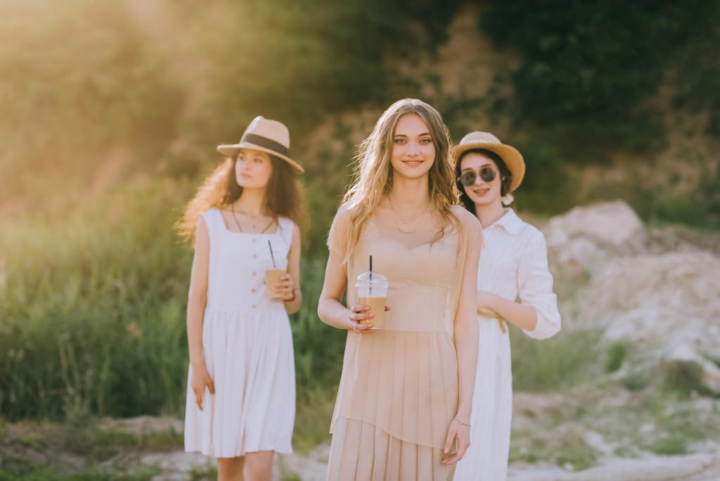 attractive girls in straw hats holding coffee latte and walking in nature with sunlight - Photo, Image