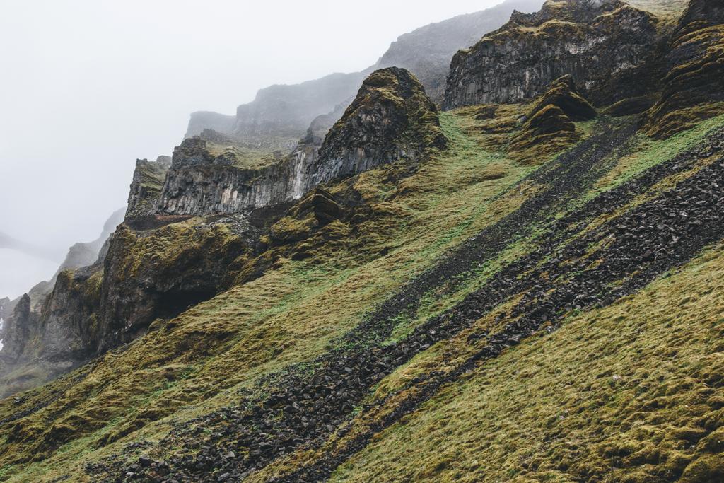 Dramatische Aufnahme eines Berges mit grünem Gras und Felsen in Island an einem nebligen Tag - Foto, Bild