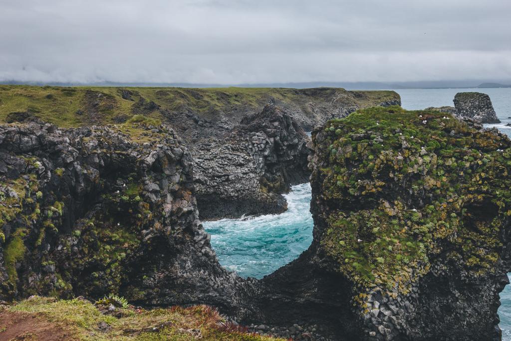 beautiful mossy cliffs in front of blue ocean in Arnarstapi, Iceland on cloudy day - Photo, Image