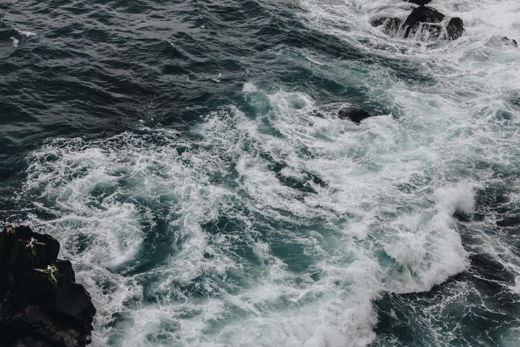 Dramatische Aufnahme schäumender Meereswellen, die im Hintergrund auf Felsen krachen - Foto, Bild