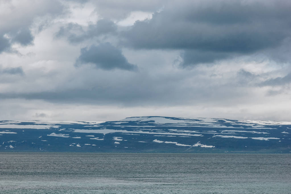 dramatic shot of lake under cloudy sky in Iceland with snowy mountains on background - Photo, Image