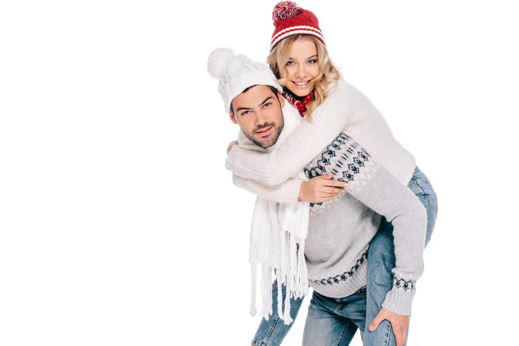 hermosa feliz joven pareja en suéteres, bufandas y sombreros a cuestas y sonriendo a la cámara aislada en blanco
 - Foto, Imagen