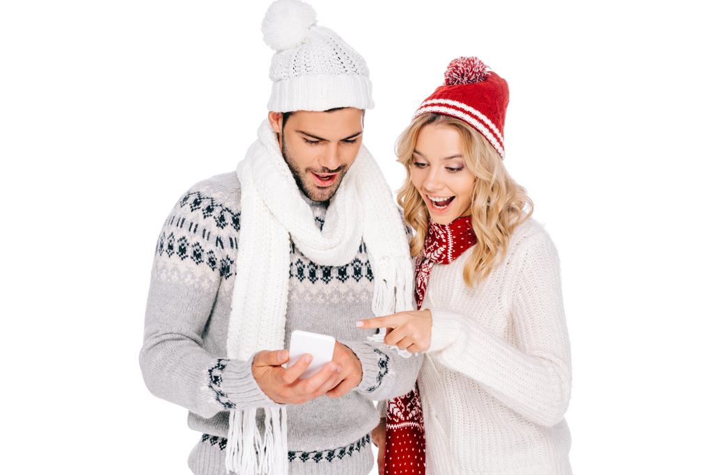 hermosa pareja joven sonriente en suéteres, bufandas y sombreros usando teléfono inteligente aislado en blanco
 - Foto, Imagen