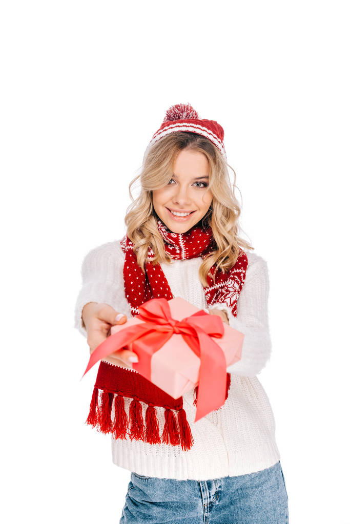 bella giovane donna in sciarpa e cappello in possesso di scatola regalo e sorridente alla fotocamera isolata su bianco
  - Foto, immagini
