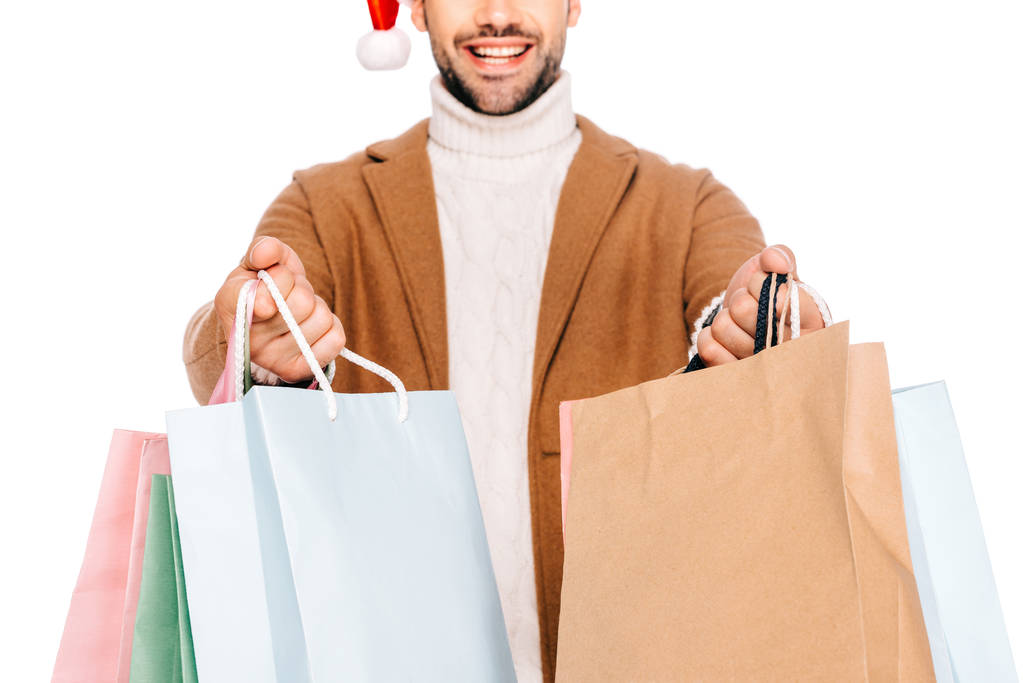 обрізаний знімок усміхненого бородатого чоловіка в капелюсі Санта, який тримає сумки для покупок ізольовані на білому
 - Фото, зображення