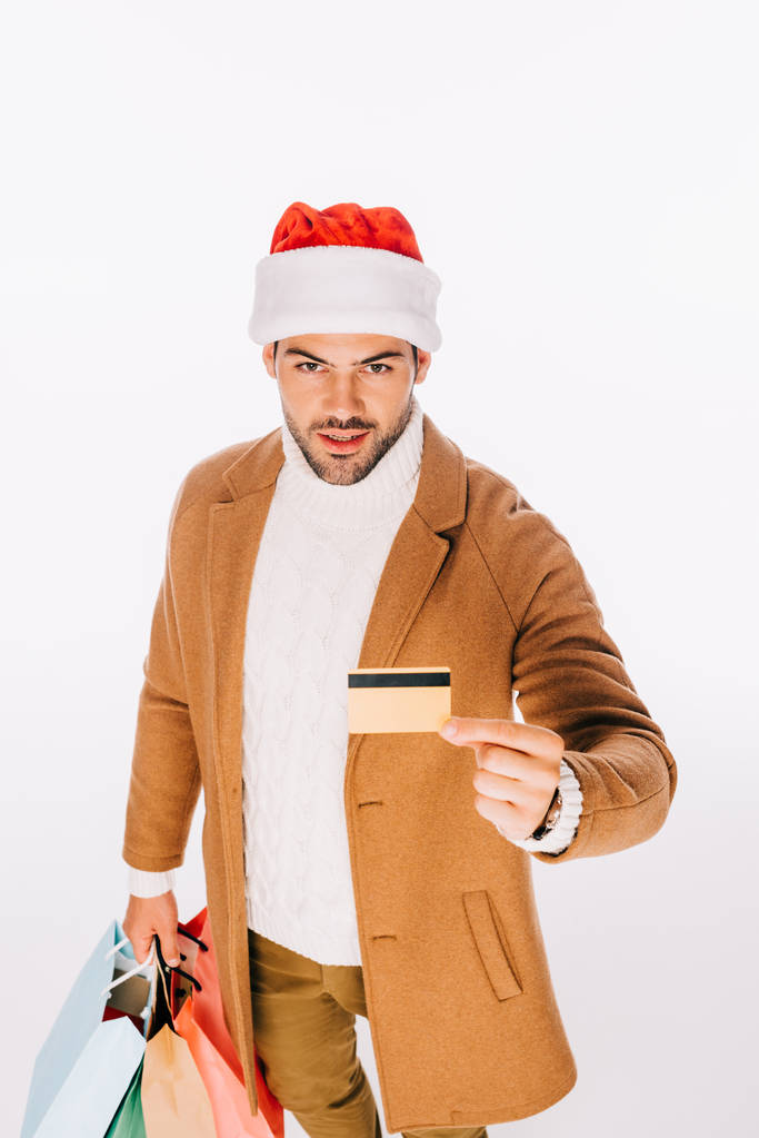 young man in santa hat holding credit card and shopping bags isolated on white - Photo, Image
