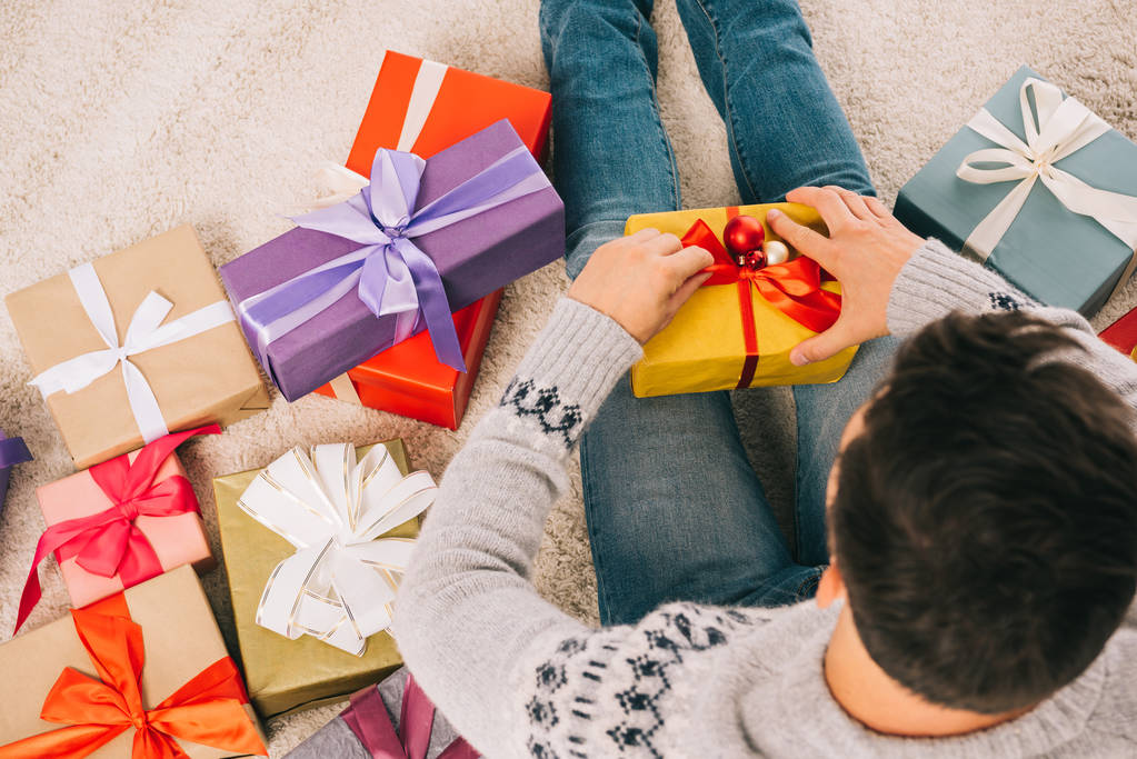 vue aérienne du jeune homme assis sur le tapis et ouvrant cadeau de Noël
 - Photo, image