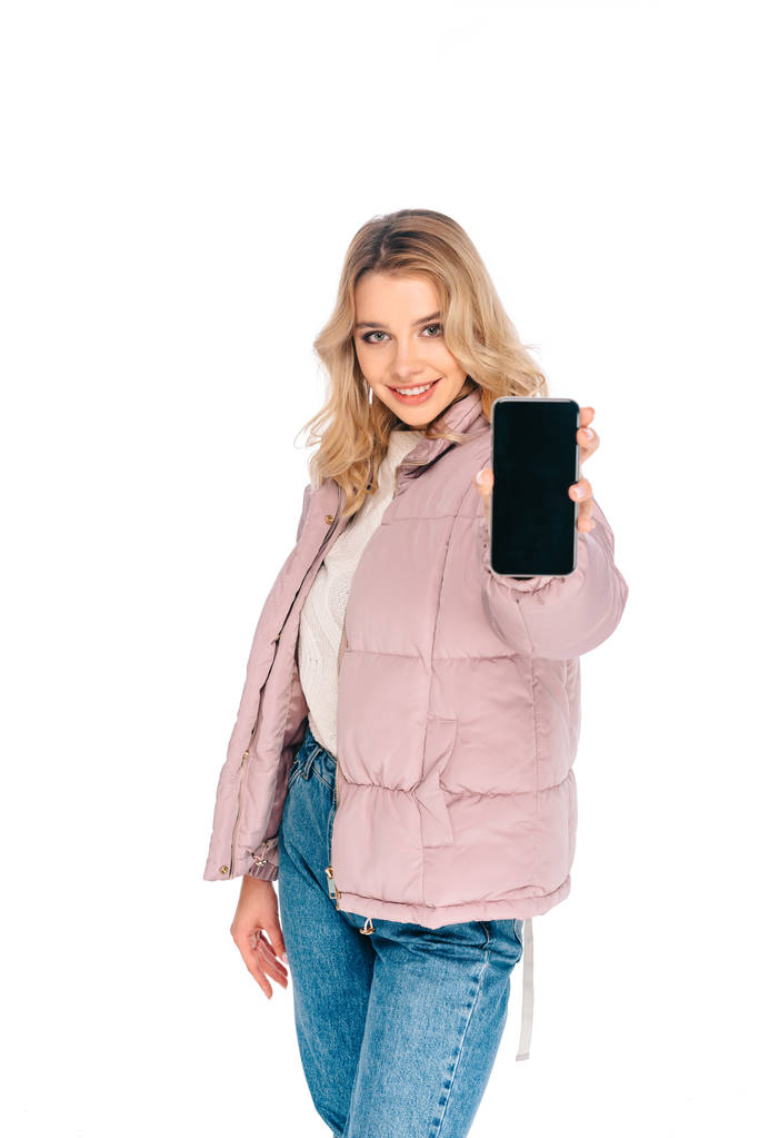 hermosa mujer joven sosteniendo teléfono inteligente con pantalla en blanco y sonriendo a la cámara aislada en blanco
  - Foto, Imagen