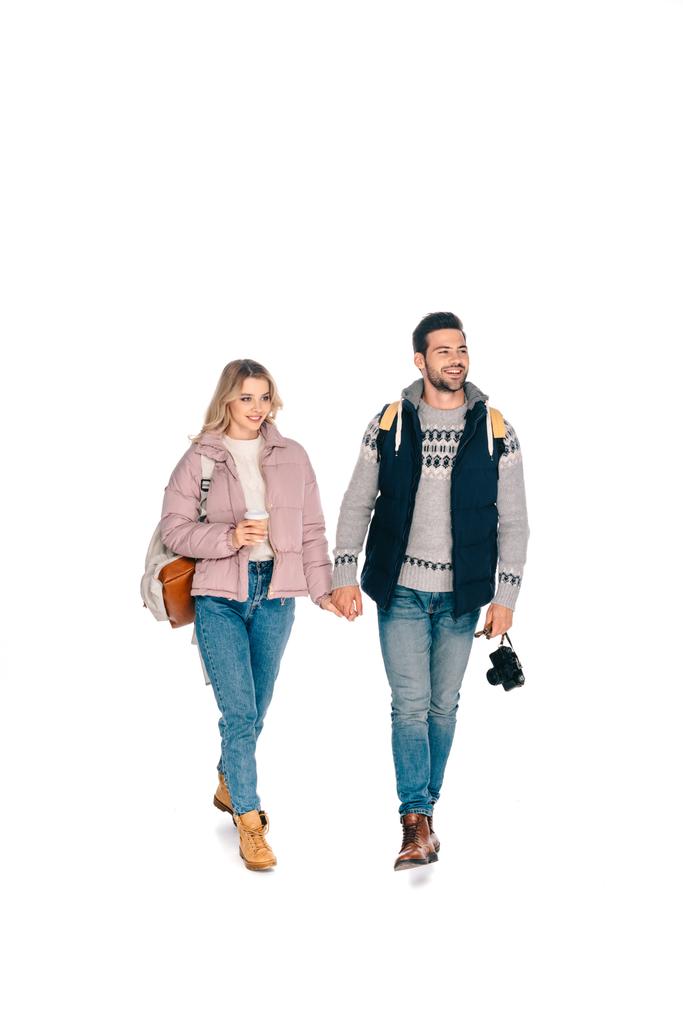 vista completa de sonriente joven pareja de turistas con mochilas sosteniendo cámara y café para ir aislado en blanco
 - Foto, Imagen