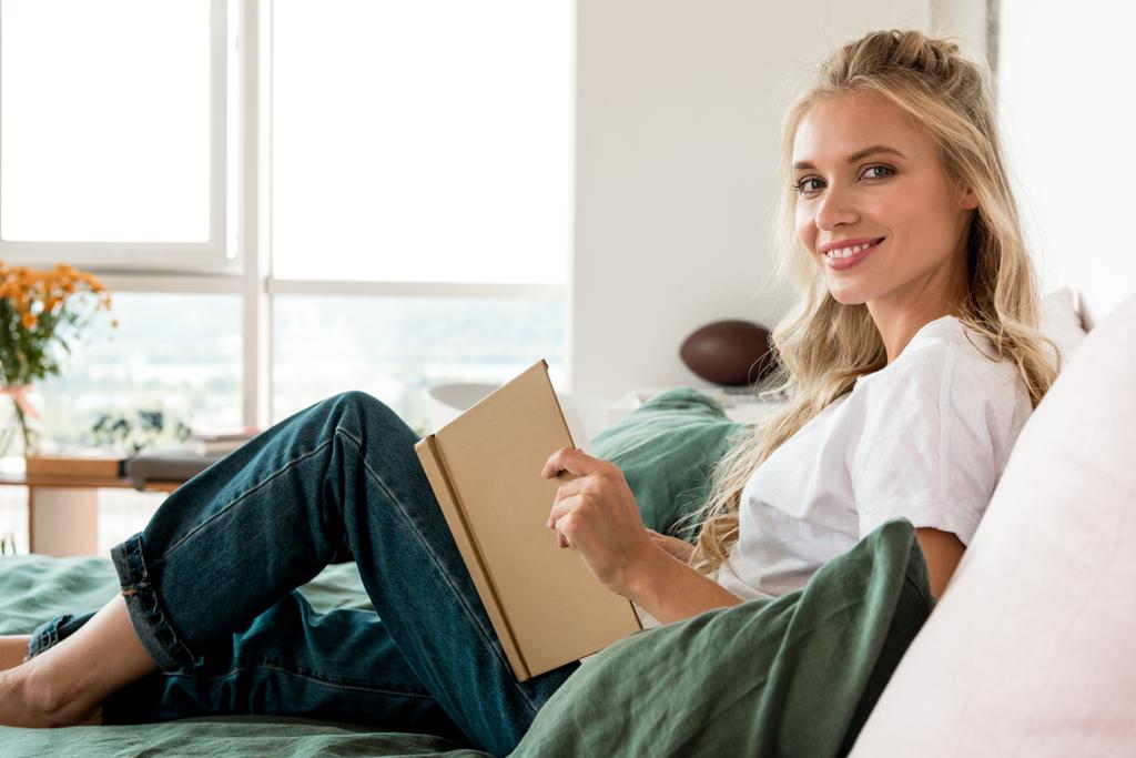 вид сбоку на молодую красивую женщину с книгой, лежащую на кровати дома
 - Фото, изображение