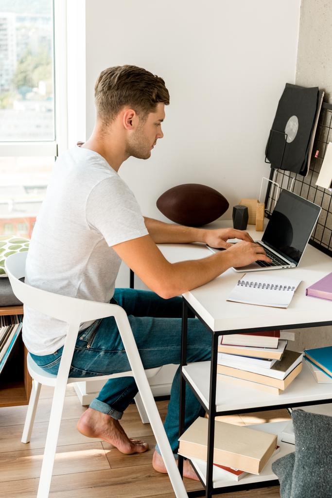 side view of young man using laptop at table at home office - Photo, Image