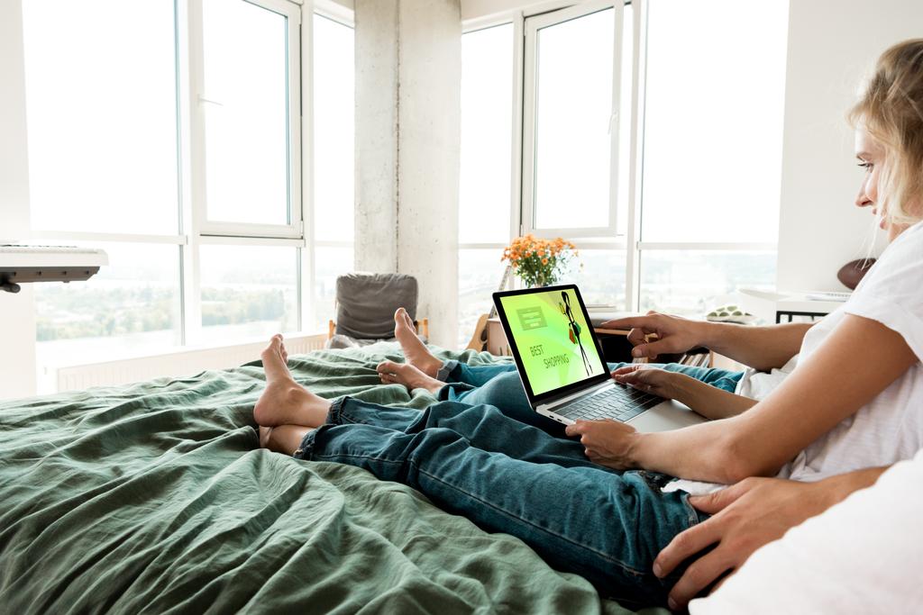 Μερική άποψη των δυο με ψηφιακό φορητό υπολογιστή με καλύτερη εμπορική γράμματα στην οθόνη ανάπαυση στο κρεβάτι στο σπίτι - Φωτογραφία, εικόνα