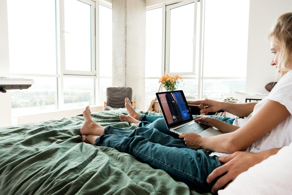 partial view of couple using digital laptop with booking sign on screen while resting on bed at home - Photo, Image