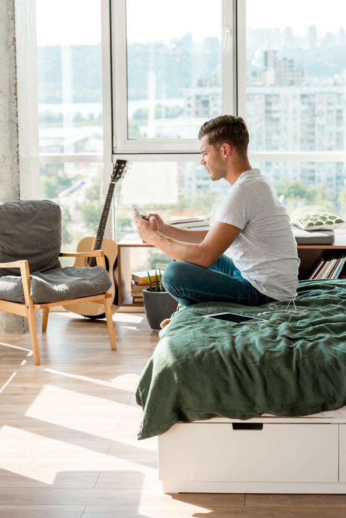 vue latérale de l'homme utilisant un smartphone tout en se reposant sur le lit à la maison
 - Photo, image