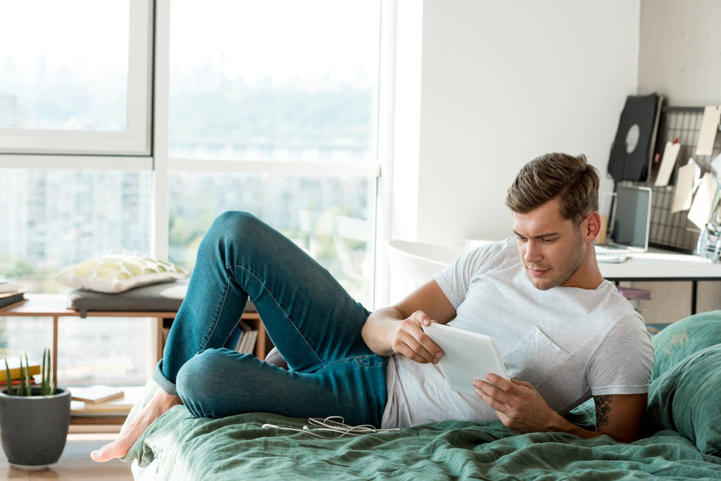 ο άνθρωπος χρησιμοποιώντας tablet ενώ ξαπλωμένος στο κρεβάτι στο σπίτι - Φωτογραφία, εικόνα