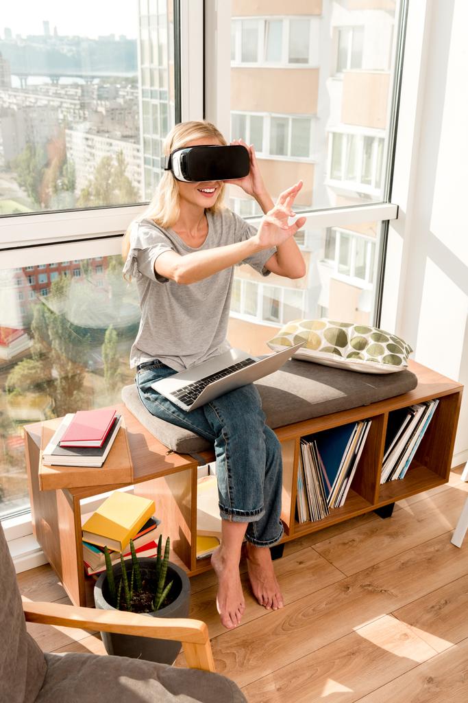 young woman in vr headset with laptop sitting at window at home - Photo, Image
