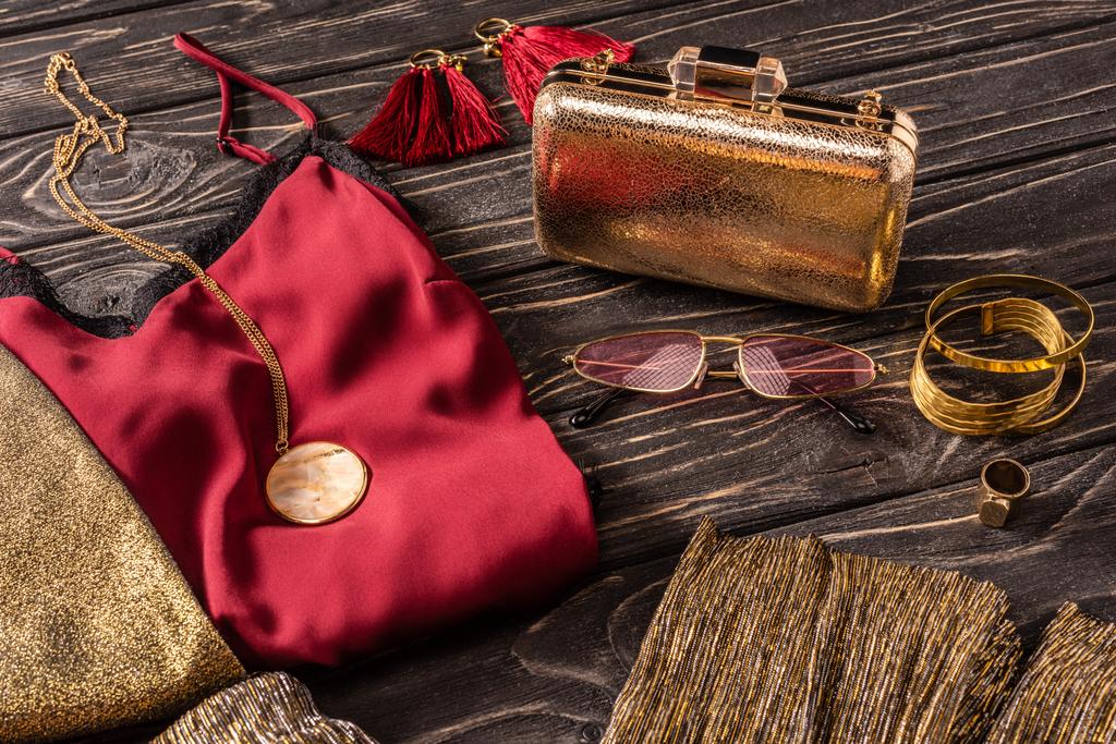 κλείνω πάνω θέα του διακανονισμού του χρυσά και κόκκινα γυναικεία αξεσουάρ μόδας και ρούχα σε ξύλινη επιφάνεια - Φωτογραφία, εικόνα