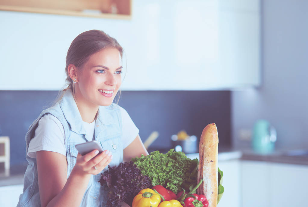 Giovane donna che tiene borsa della spesa con verdure. In piedi in cucina - Foto, immagini