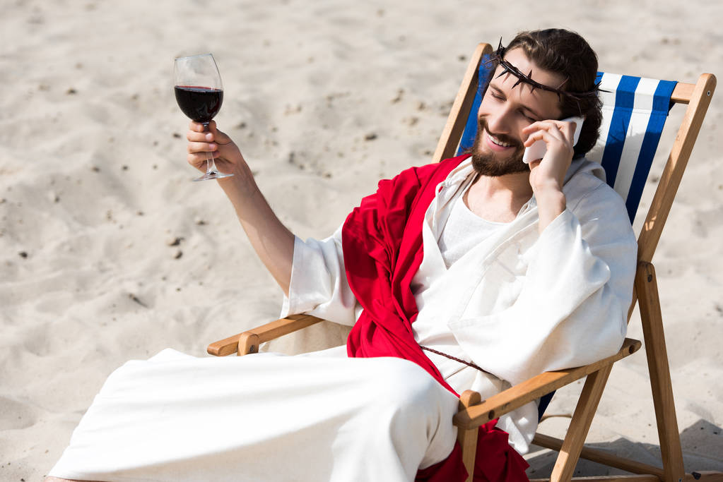 mosolygós Jézus pihen a nyugágyon, pohár bor, és beszél a smartphone-sivatagban - Fotó, kép