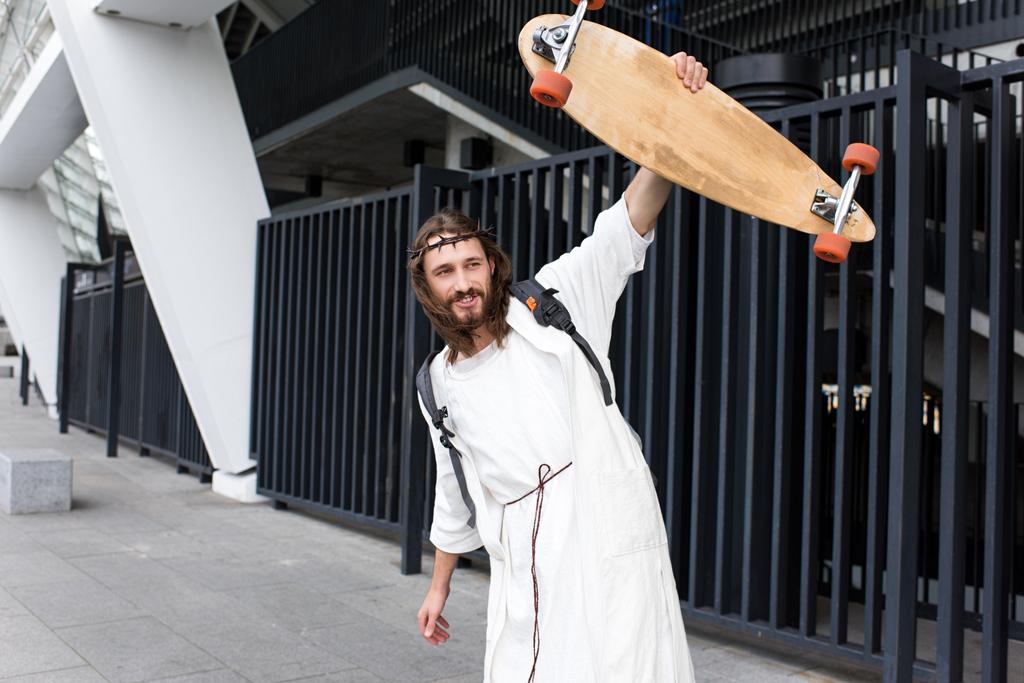 Jesús alegre en túnica, corona de espinas y bolso mostrando monopatín en la calle
 - Foto, imagen