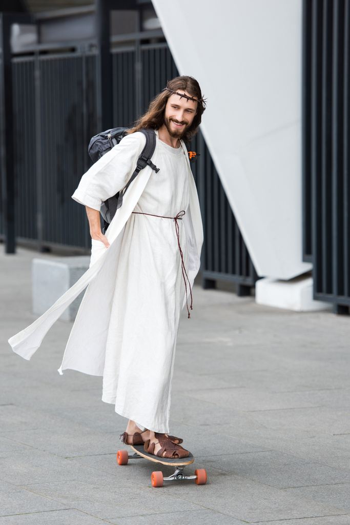 Улыбаясь, Иисус в мантии и терновом венце катается на коньках на длинной доске по улице
  - Фото, изображение