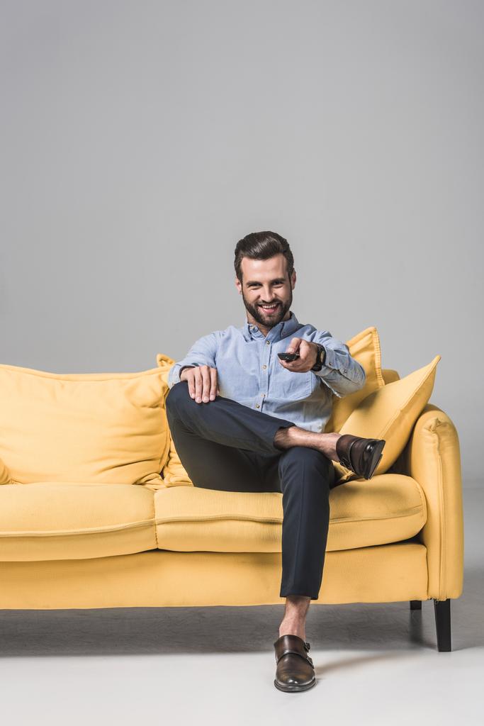 Tv izlerken, gri sarı koltukta oturan kumanda ile neşeli sakallı adam - Fotoğraf, Görsel