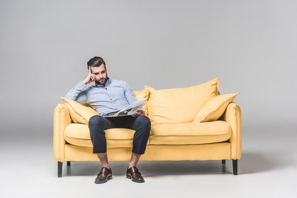 αναστατώσει επιχειρηματίας διαβάζοντας εφημερίδα ενώ κάθεστε στον καναπέ, κίτρινο, σε γκρι - Φωτογραφία, εικόνα