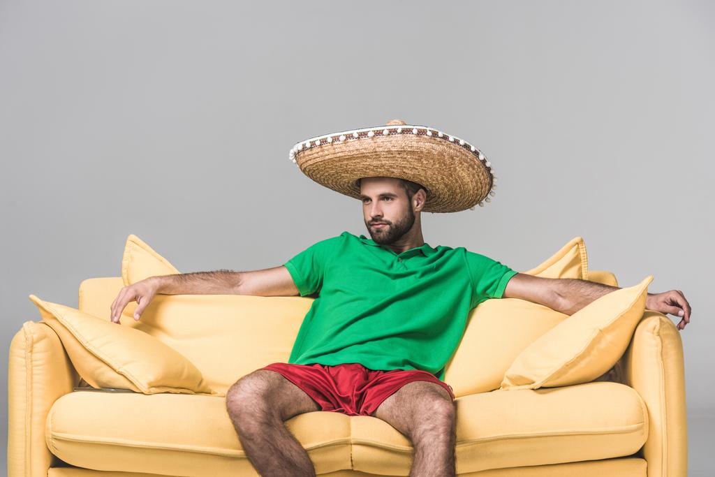 handsome mexican man in sombrero on yellow sofa on grey  - Photo, Image