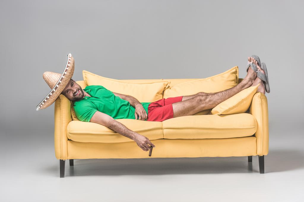 グレーで葉巻と黄色のソファーで休んでメキシコのソンブレロで幸せな男  - 写真・画像