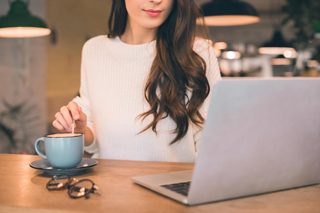 gedeeltelijke weergave van vrouwelijke freelancer zitten met laptop en koffie kopje aan tafel in café - Foto, afbeelding