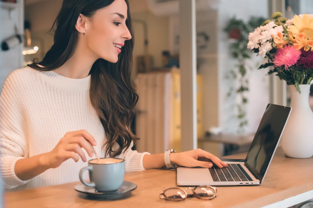 vue latérale de belle pigiste féminine travaillant sur ordinateur portable à la table avec tasse de café dans le café
  - Photo, image