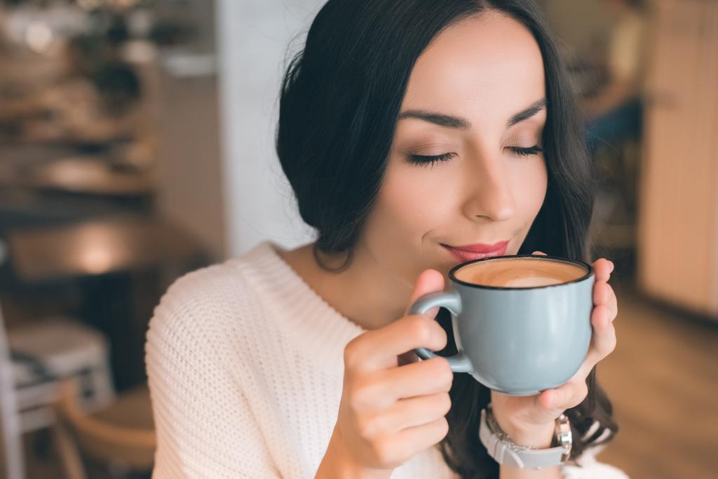 Portret van de jonge vrouw close-up met gesloten ogen koffie drinken in café - Foto, afbeelding