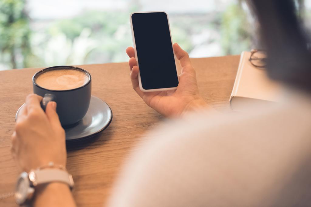 vista parziale della donna con tazza di caffè utilizzando smartphone a tavola nel caffè
 - Foto, immagini