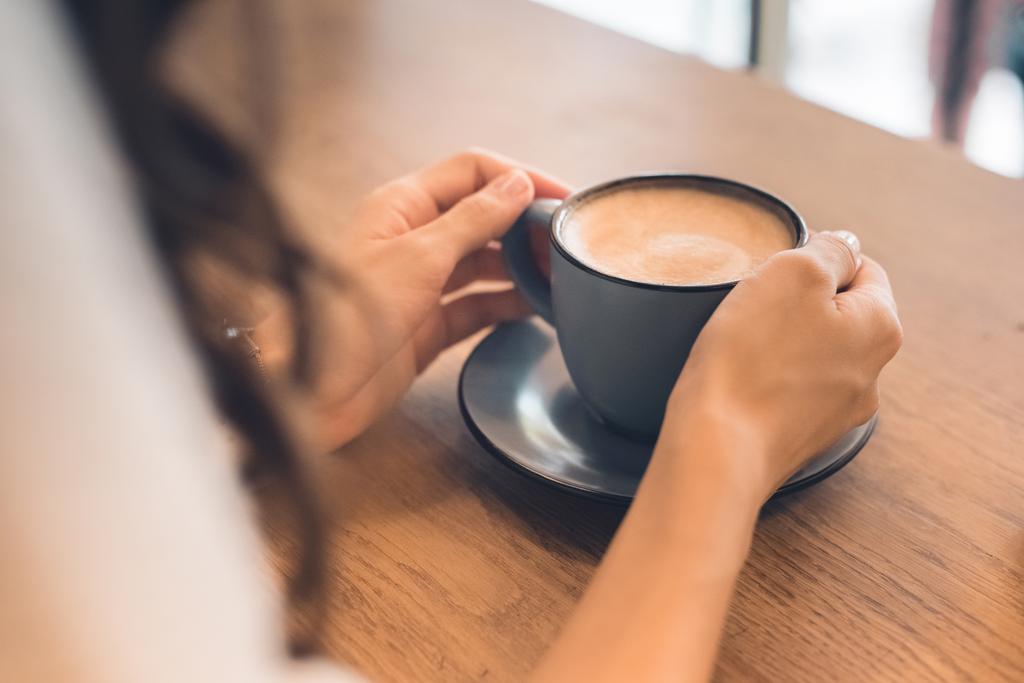 vista parcial de la mujer sentada con taza de café en la mesa en la cafetería
 - Foto, Imagen