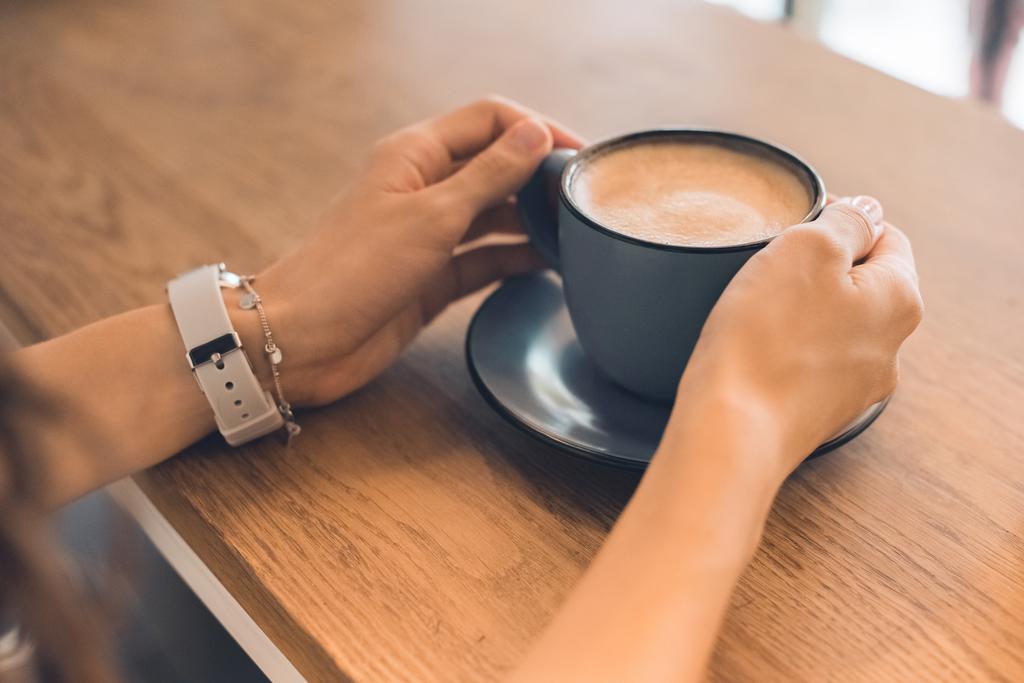 περικομμένη εικόνα γυναίκα κάθεται με φλιτζάνι καφέ στο τραπέζι στην καφετέρια - Φωτογραφία, εικόνα