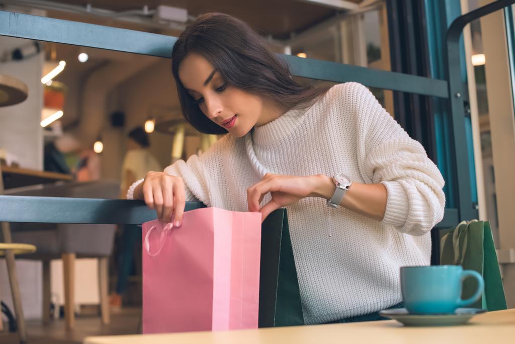 focalizzata giovane donna in cerca di shopping bag a tavola nel caffè
 - Foto, immagini