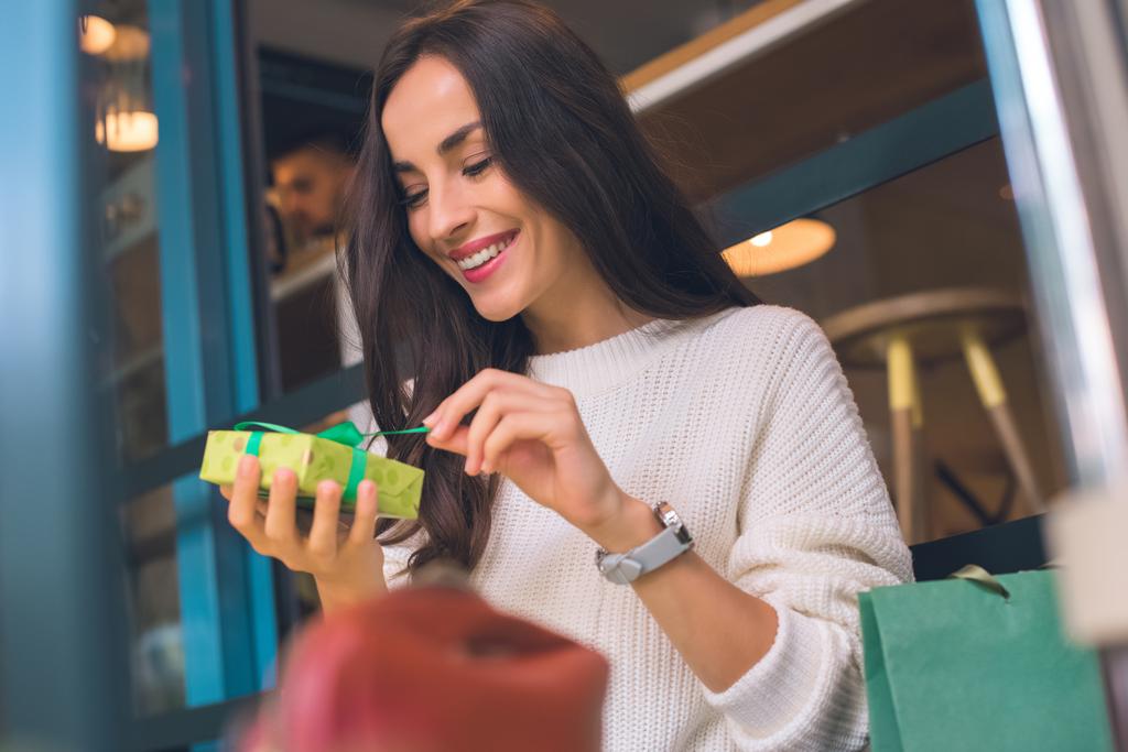 sonriente joven mujer desatando caja de regalo en la cafetería
 - Foto, Imagen