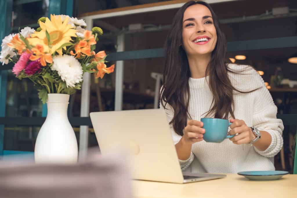 glückliche Freiberuflerin mit Kaffeetasse sitzt am Tisch mit Laptop im Café - Foto, Bild