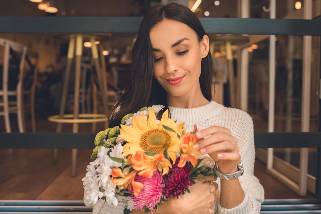 όμορφη νεαρή γυναίκα κρατώντας πολύχρωμο μπουκέτο από διάφορα λουλούδια σε καφέ - Φωτογραφία, εικόνα