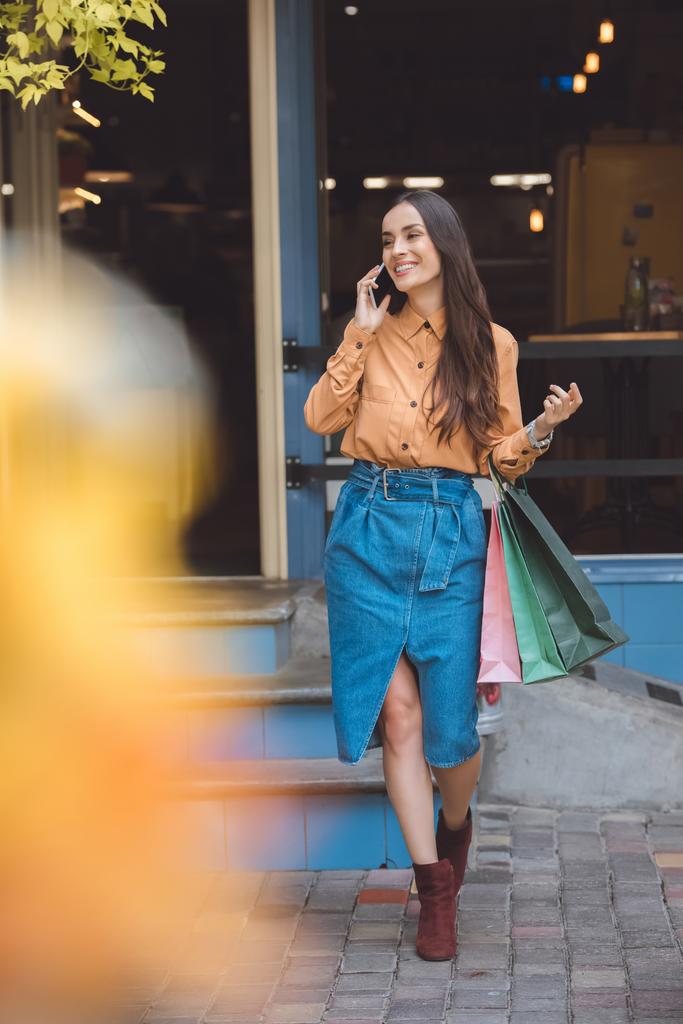молодая стильная женщина с сумками для покупок разговаривает по смартфону на городской улице
 - Фото, изображение