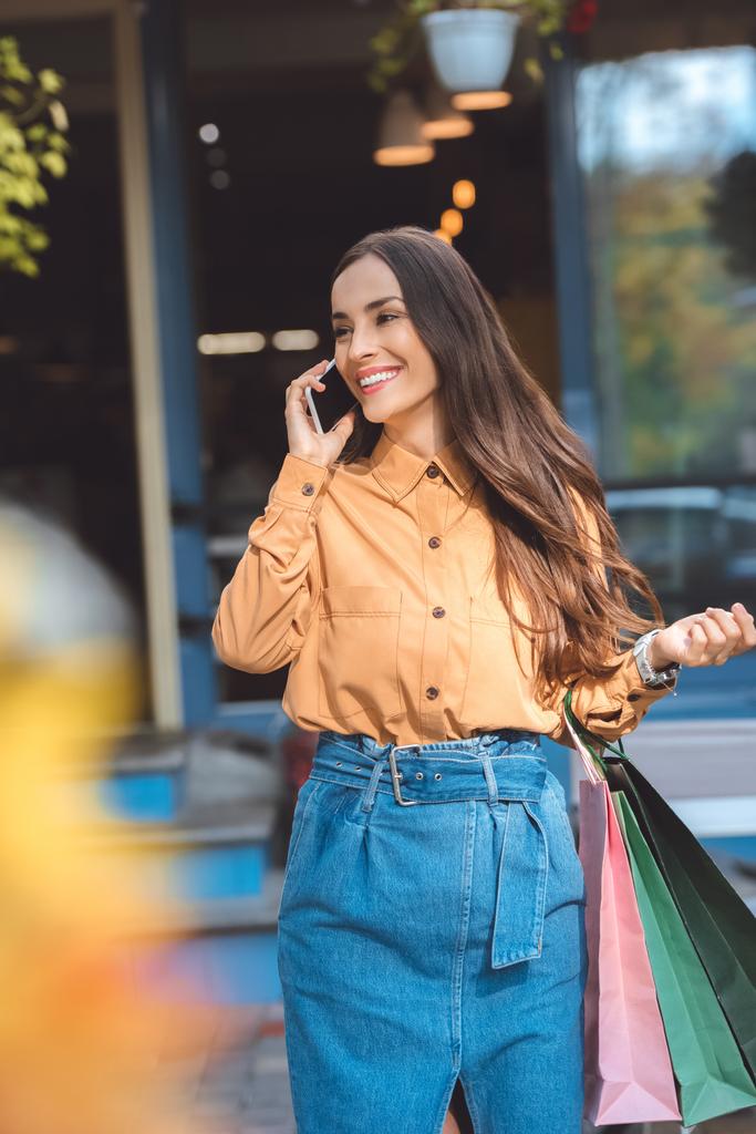 feliz mujer joven con estilo con bolsas de compras hablando en el teléfono inteligente en la calle de la ciudad
 - Foto, imagen
