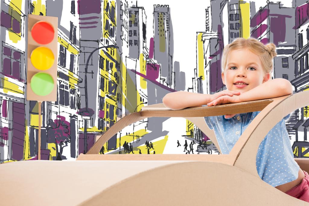 adorable child playing with cardboard car and traffic lights on street in drawn city - Photo, Image