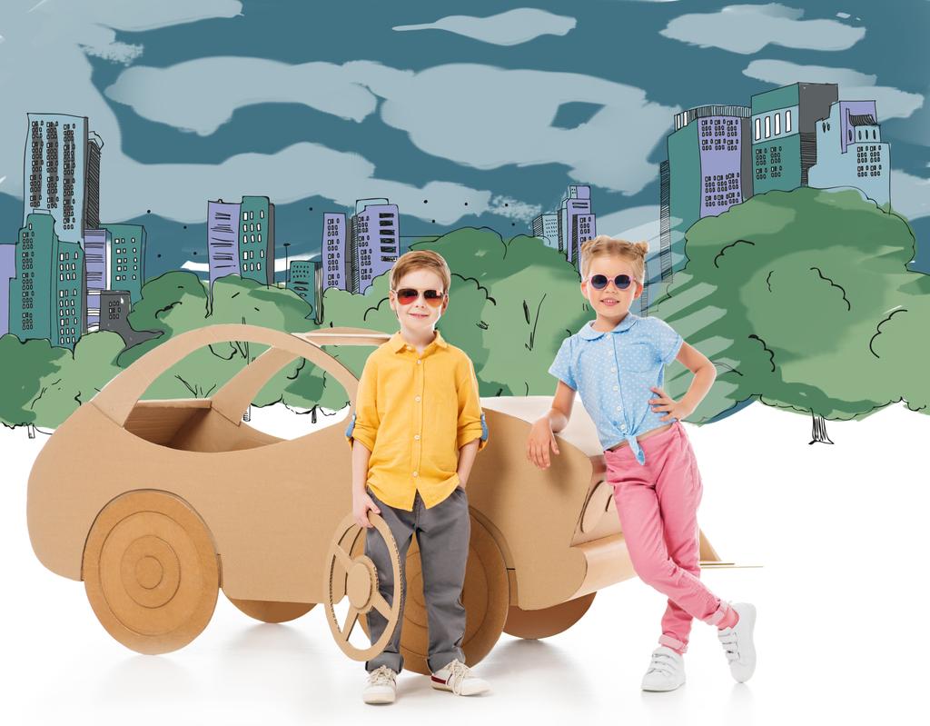 стильные дети в солнечных очках позируют рядом с картонным автомобилем в рисованном городе и парке
 - Фото, изображение