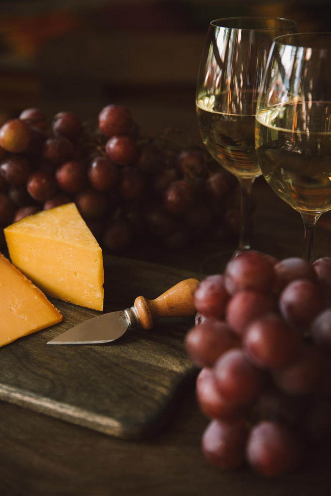 крупним планом шматок нарізаного сиру з ножем, виноградом та білим вином на обробній дошці
 - Фото, зображення