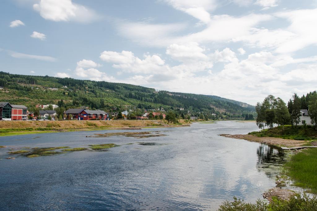 distant view of buildings on river shore with green hill, Trysil, Norway's largest ski resort  - Photo, Image