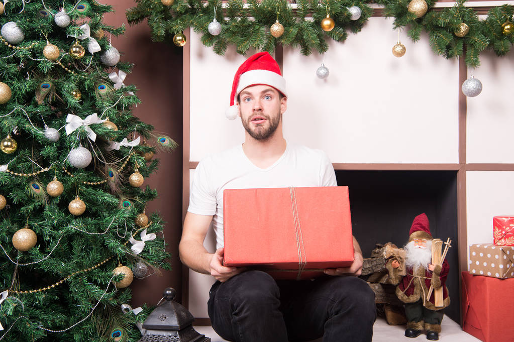 Weihnachtsmann mit überraschtem Gesicht hält Geschenk am Weihnachtsbaum - Foto, Bild