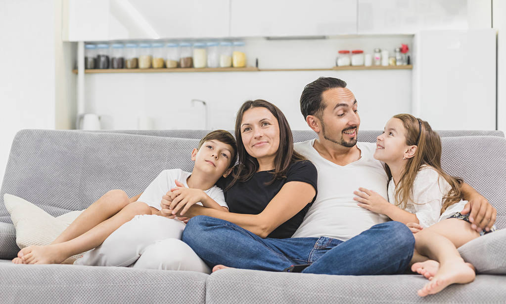 Семья, сидящая на диване, улыбается перед камерой на фоне современной квартиры
 - Фото, изображение